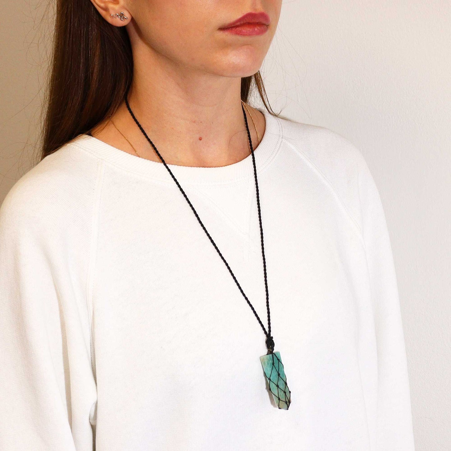 Person wearing a necklace with a green pendant against a plain background